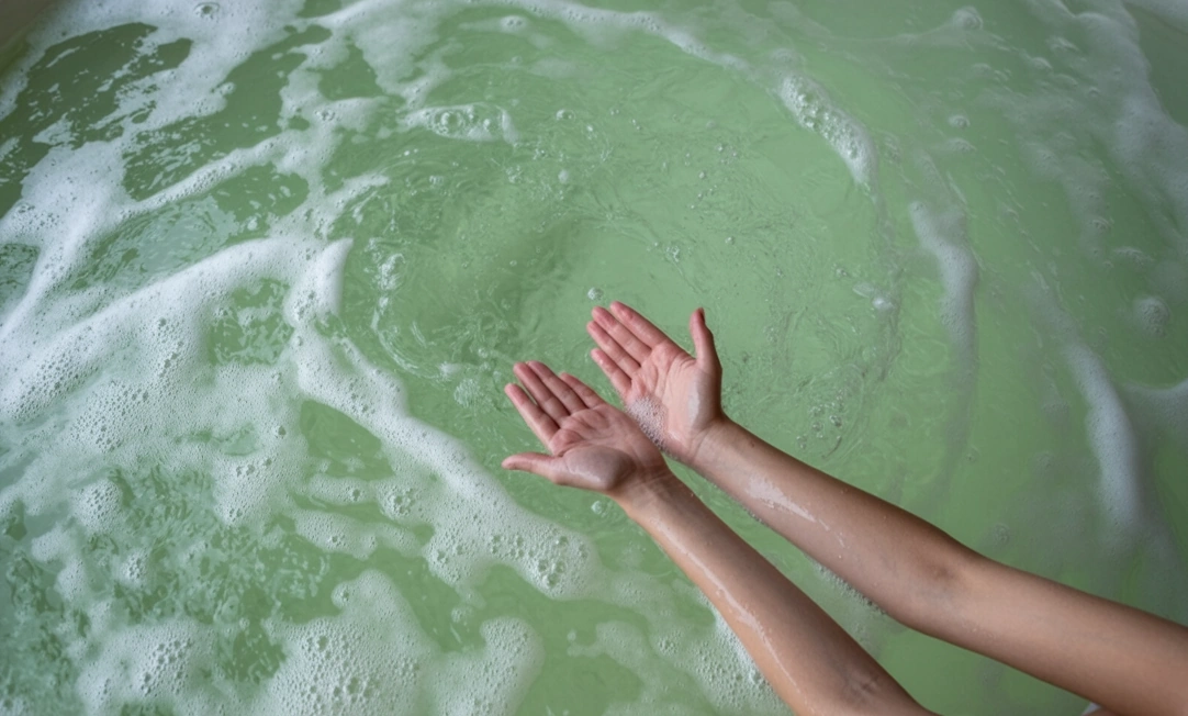 hands reaching down into a foamy, light green-colored water in a hot tub
